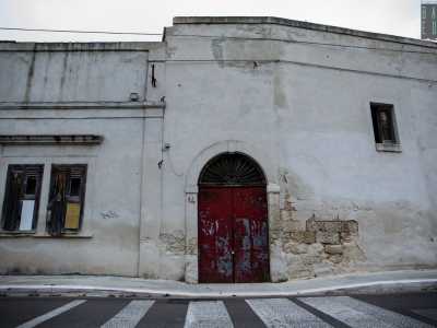 La struttura presenta al centro un arco in pietra che racchiude il rosso portone di ingresso serrato da un lucchetto...